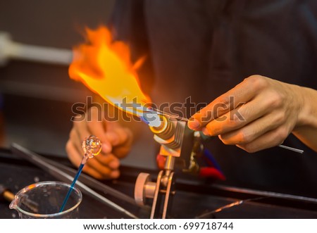 close up image of hand holding glass rod on glassblower flame in glassware making factory.