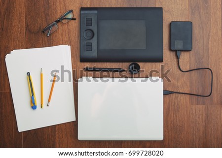 Flat lay of office equipment for working with laptop, graphic tablet, paper, pencils, glasses. Small illustration business. View from top above overhead. Freelance workplace concept