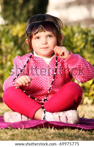 A picture of a cute baby girl putting on a lip gloss and playing with mum's necklace in the park