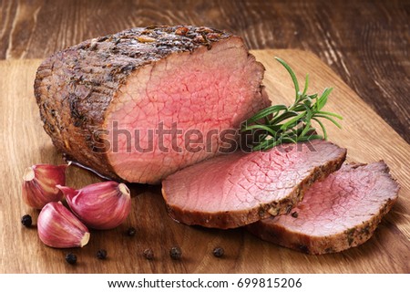 Baked meat, garlic and rosemary on a wooden background. Roast beef. Royalty-Free Stock Photo #699815206