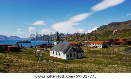 Remains of early 19th century Norwegian whaling settlement with rusting tanks, abandoned buildings and restored Lutheran church. Grytviken, South Georgia Island, South Atlantic Ocean. Royalty-Free Stock Photo #699817975