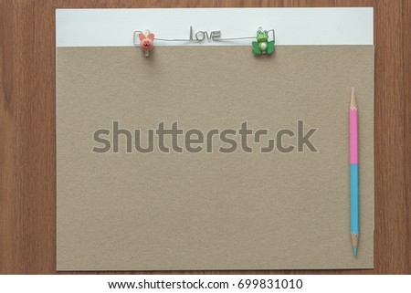 Brown card with pink and blue pencil color on the wooden background, blank note in brown board and wire in love text with pig and frog cartoon