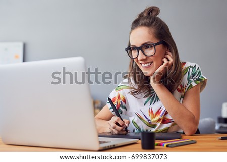 Beautiful smiling young graphic designer sitting at desk in office and working