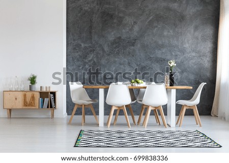 White flowers in black vase next to glass container with wine corks on dining table Royalty-Free Stock Photo #699838336