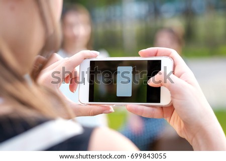 Back view of a young girl taking photo with a smart phone camera of a blurred friends and see error message. Copy space