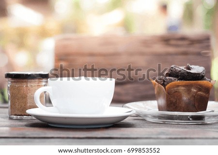 Blurry picture of a cup of coffee and a jar of brown sugar with a piece of chocolate muffin on the wooden table in the morning time