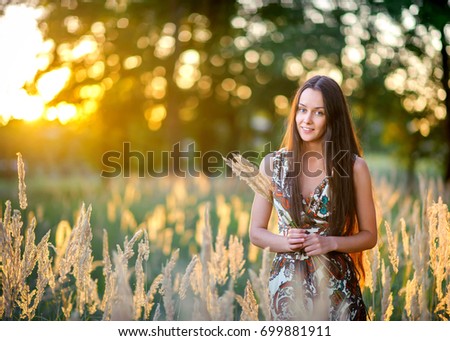 beautiful young girl walks in the park on a sunset, collects a bouquet from field herbs