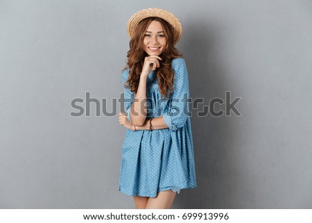 Picture of happy young pretty woman standing over grey wall wearing hat. Looking camera.