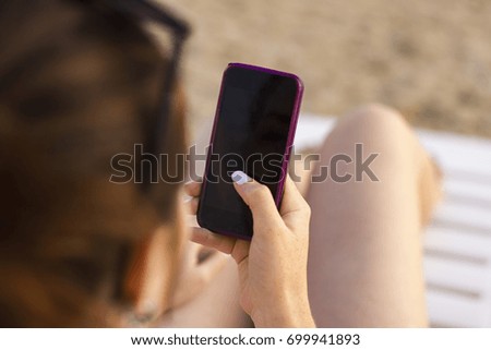 A young girl is holding a smart phone, a blank screen template. Summer trip on the beach with a phone.