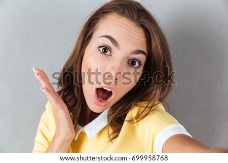 Close up of surprised pretty girl taking a selfie isolated over gray background