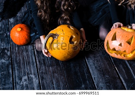 girls sitting with the Halloween pumpkin head jack lantern on dark wooden background, concept of a holiday Halloween