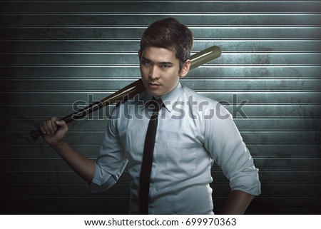 Young asian man with wooden baseball bat standing against dirty background