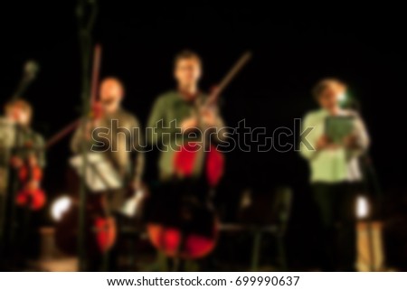 Background for design, blur texture, actors on stage scene in concert with silhouettes of people. De focused/ Blurred image of the conductor introducing musical composition before performance. 