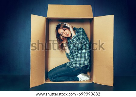 Introvert concept. Woman sitting inside box and with headphones