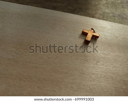 Old Christian cross placed on wooden background in morning sunlight, selective focus with copy space