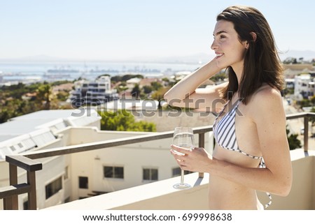 Brunette babe in bikini relaxing with wine on balcony, smiling
