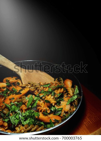 The picture of homemade fusilli with roasted chili paste and sausage on pan above wooden table.  black background