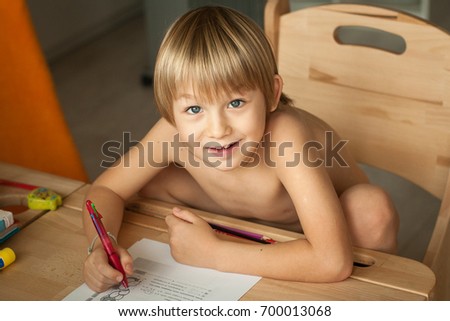 Young boy of school age sitting near the wooden desk looking up with pen in his hand and writing test