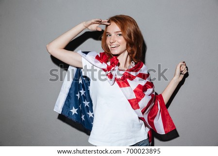 Picture of happy redhead young lady superhero with USA flag. Looking camera.