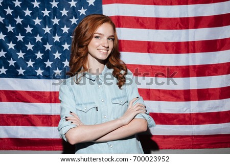 Picture of happy redhead young lady standing over USA flag. Looking camera.