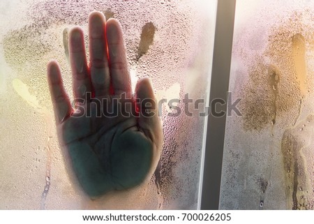 Silhouetted palm of hand, behind the window, selective focus on drop water and surface on glass. Scream for help, halloween day, depression, stress, panic concept.