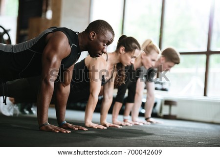 Picture of group of multiethnic sports strong people make sport exercises in gym.