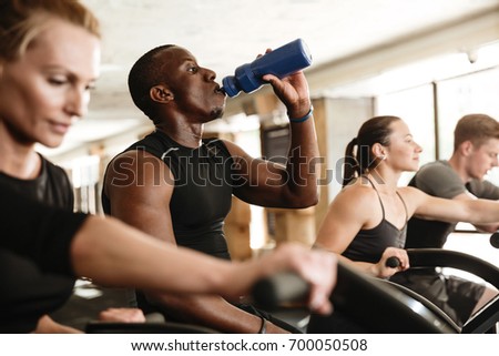 Picture of group of multiethnic sports strong people make sport exercise with spinning bicycles drinking water.