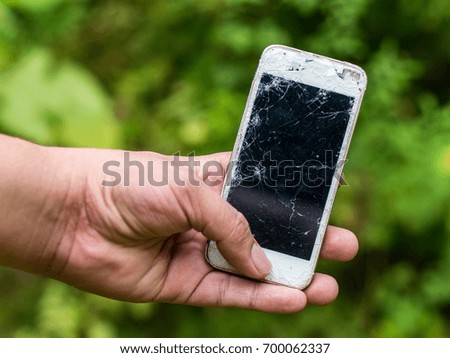 Man's hand holding a broken mobile phone with green nature background