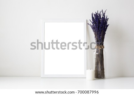 Beautiful cozy shot of white table in living room or home office desk with glass vase or bottle with dried lavender flowers, candle and empty picture frame with copy space for your photograph