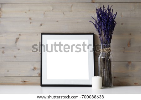 Close up picture of foursquare space photo frame with copy space, white paraffin candle and glass vase with dried lavender flowers in it. Ideas for interior, decor, decoration and design concept