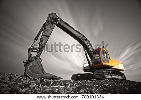 Excavator parked on stone ground against dramatic sky Royalty-Free Stock Photo #700101334