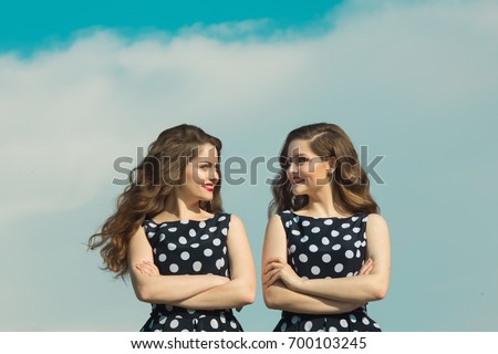 Two beautiful sisters twin girls in identical dresses, with makeup and hairdo on blue sky background Royalty-Free Stock Photo #700103245