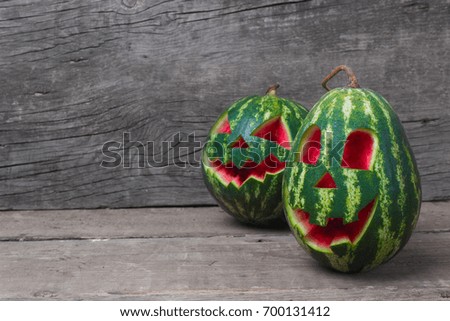 Watermelon with a smiling face like a pumpkin for Halloween. Wooden table and old boards. Empty space for text.