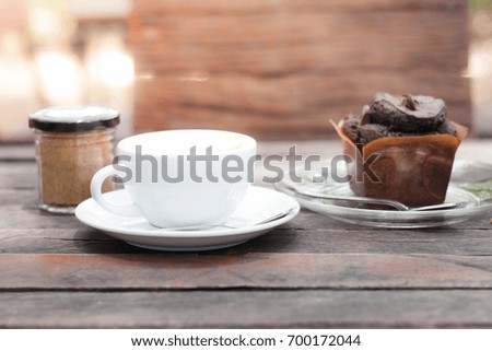 Blurry picture of a cup of coffee and a jar of brown sugar with a piece of chocolate muffin on the wooden table