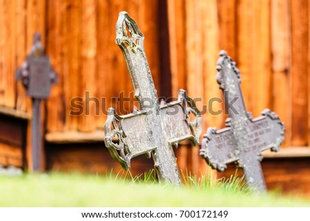 Old metal crosses with wooden church wall in background. Low angle with green grass in foreground.