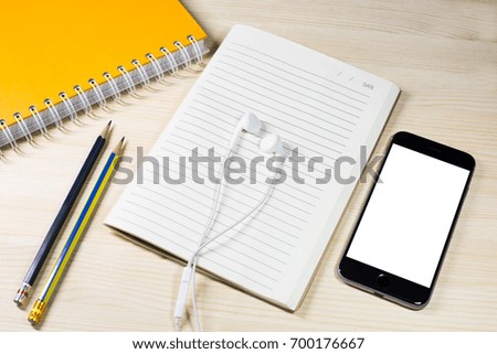 Top view of the office table with earphone on blank notebook and blank phone is white color desktop