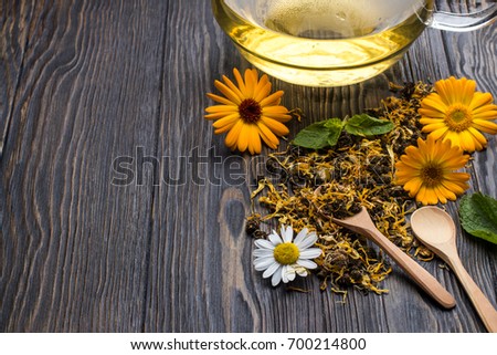 herbal tea with calendula and mint are scattered on wooden background. Spoon with tea, kettle with tea. Ivan-tea