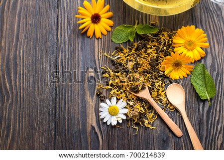 herbal tea with calendula and mint are scattered on wooden background. Spoon with tea, kettle with tea. Ivan-tea