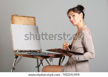 A young woman near easel begins to draw a picture.