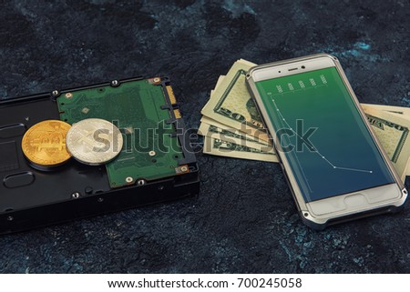 Bitcoin coins with HDD, money and smartphone with diagrams on screen on a dark background