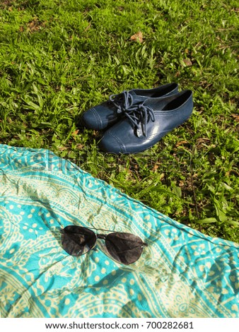 Sunglasses on picnic cloth and feminine blue shoes on the grass - relaxing day at the park