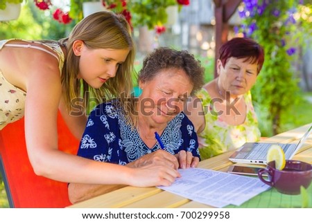 Pensioner signing  legacy heritage testament document near a  witness for her granddaughter. Royalty-Free Stock Photo #700299958