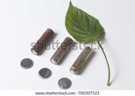 Waste batteries of different types are scattered. Nearby is a green juicy leaf. On a white background. View from above. Disposal of environmentally hazardous waste. Protection of the environment.