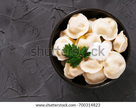 Traditional russian pelmeni, ravioli, dumplings with meat on black concrete background. Copyspace. Top view or flat lay. Russian food and russian kitchen concept.