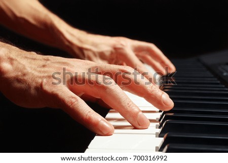 Hands of composer play the keys of the piano on a black background close up