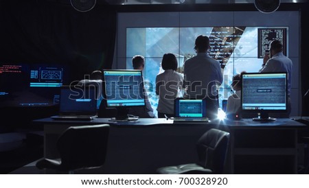 Back view of people working and managing flight in mission control center. Elements of this image furnished by NASA. Royalty-Free Stock Photo #700328920