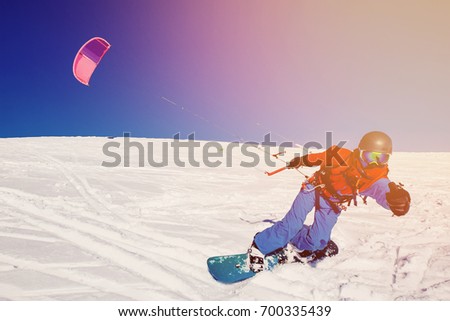 Snowboarder with a kite on fresh snow in the winter in the tundra of Russia against a clear blue sky. Teriberka, Kola Peninsula, Russia. Concept of winter sports snowkite. Royalty-Free Stock Photo #700335439