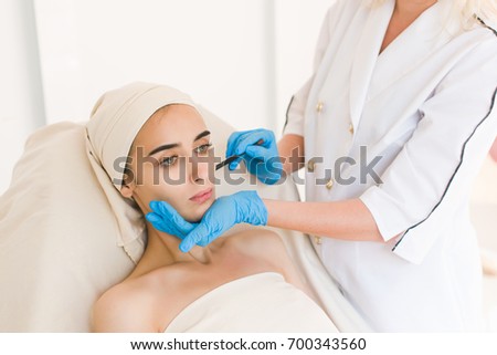 Plastic surgery concept. Doctor drawing marks on female face against white background