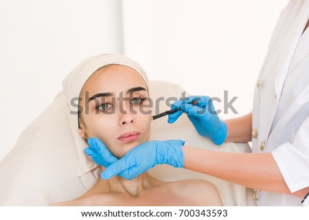 Plastic surgery concept. Hand in blue glove marking women face against white background.