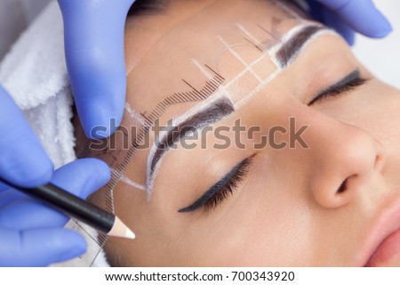 Permanent make-up for eyebrows of beautiful woman with thick brows in beauty salon. Closeup beautician doing  tattooing eyebrow. Royalty-Free Stock Photo #700343920